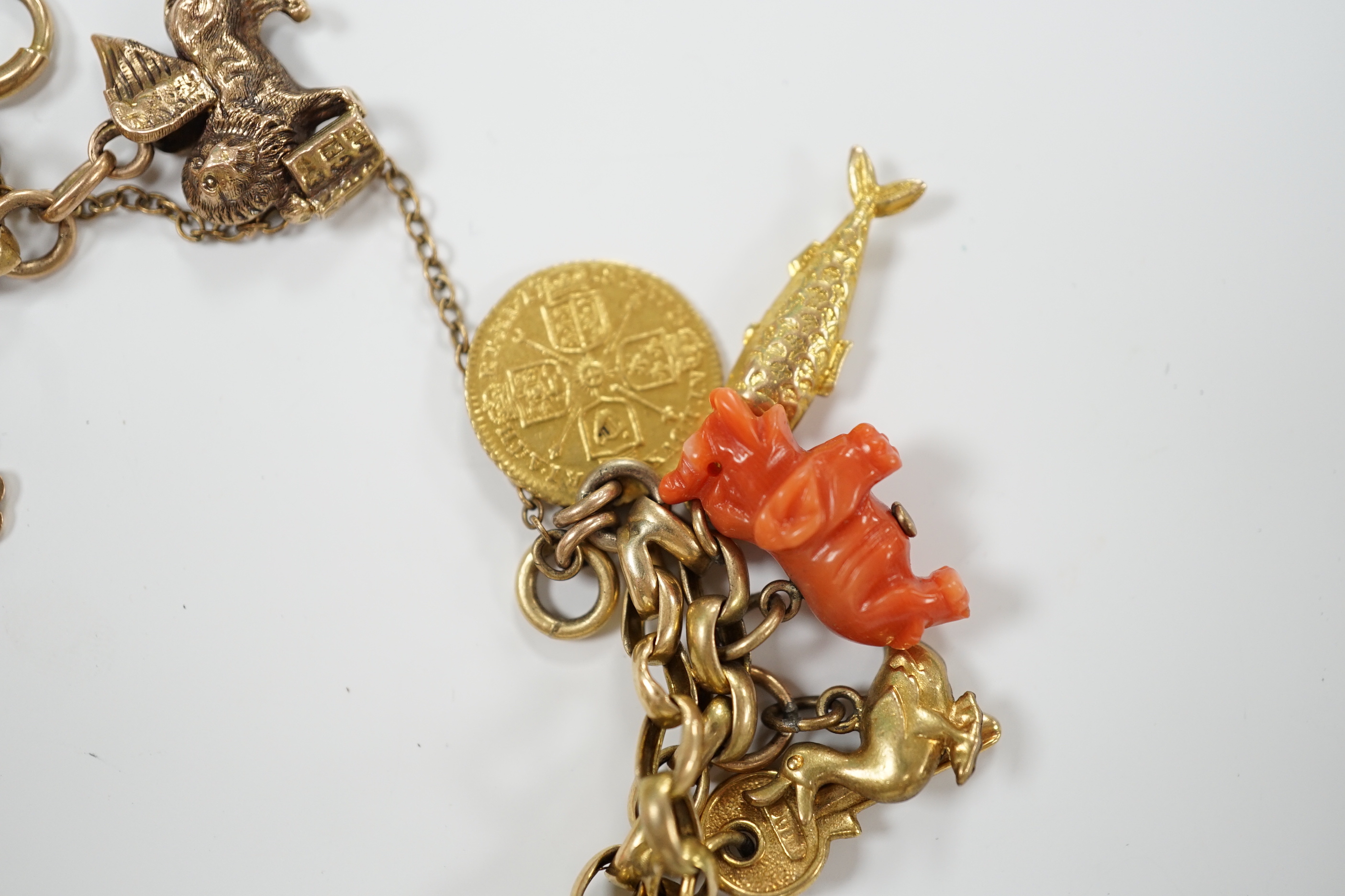 An early 20th century 9ct multi link charm bracelet, hung with sixteen assorted charms, including 9ct, coral, enamelled and a worn spade guinea